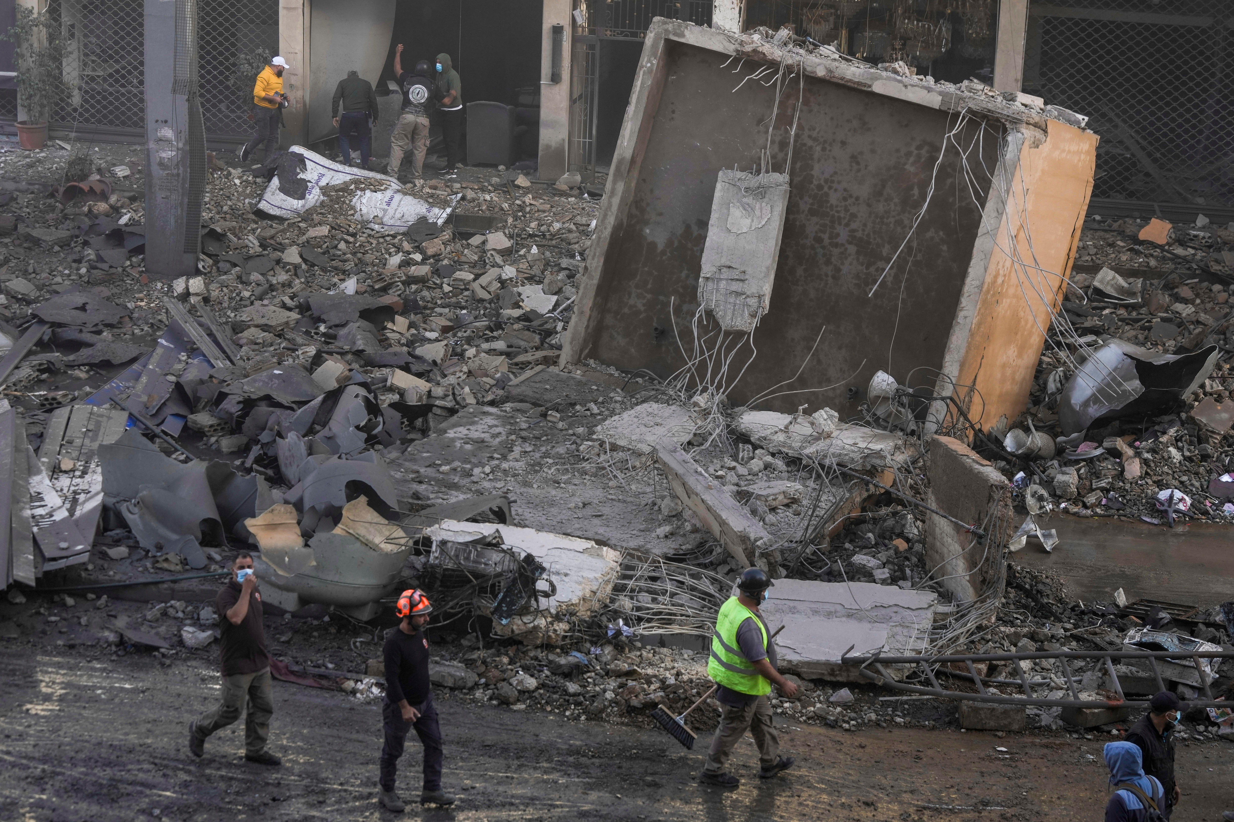 Rescue workers wearing hi-viz vests and helmets walking alongside a large pile of building debris