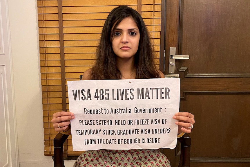 A lady with a patterned dress holding a sign saying 'VISA 485 LIVES MATTER'