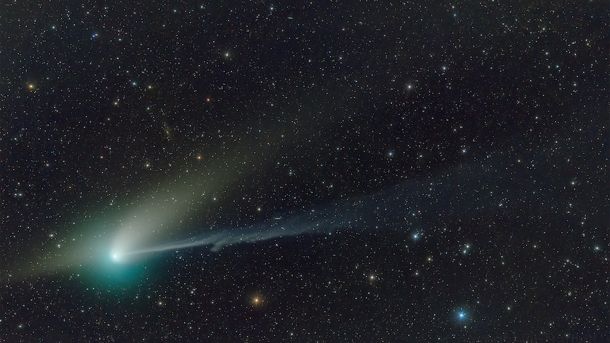 A comet emits a green glow against a blanket of stars in the night sky