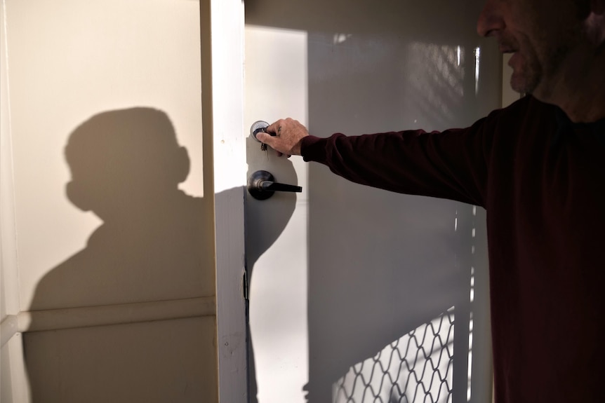 The shadow of a man displays over the front door as he turns the lock with a key