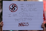 A protest sign reads 'I can't believe I am still protesting Nazis'