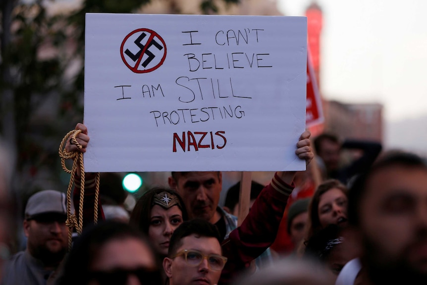 A protest sign reads 'I can't believe I am still protesting Nazis'