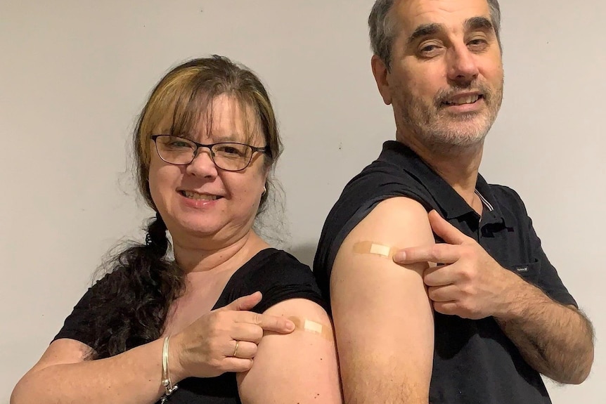 A man and a woman stand back-to-back and show off their vaccine marks.