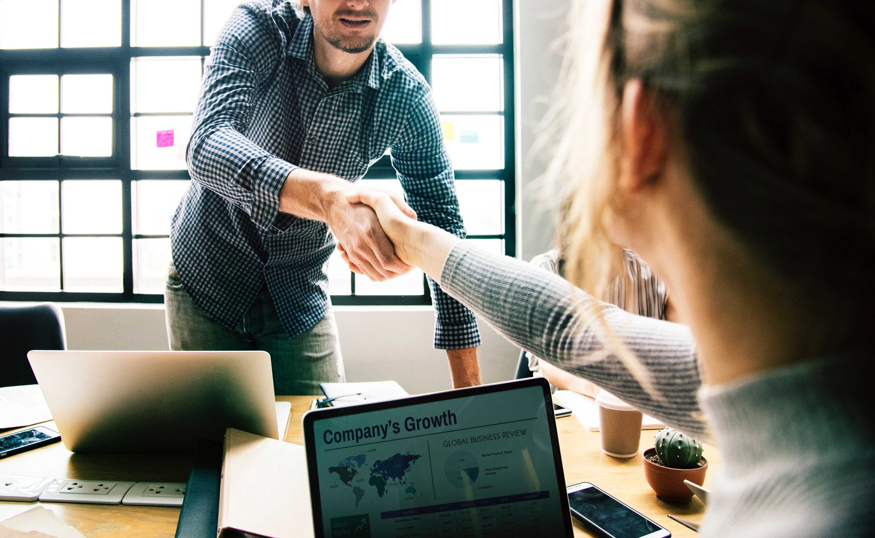 A man shaking a woman's hand over their computers