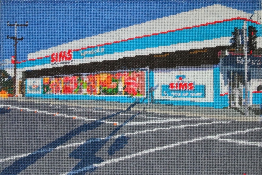 Needlepoint depiction of a supermarket building, with bright blue and red design, and shadows across a road before it.