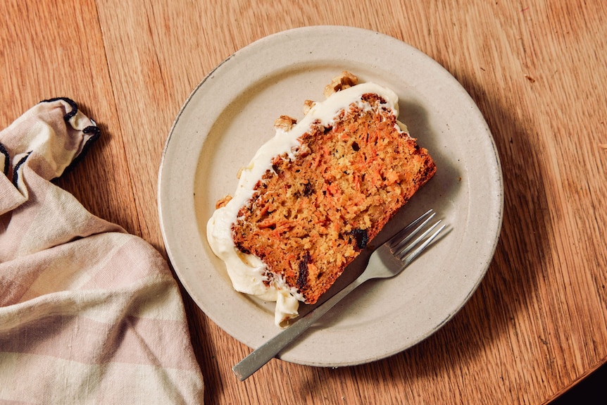 A slice of carrot cake with thick cream cheese frosting, on a plate with a fork.