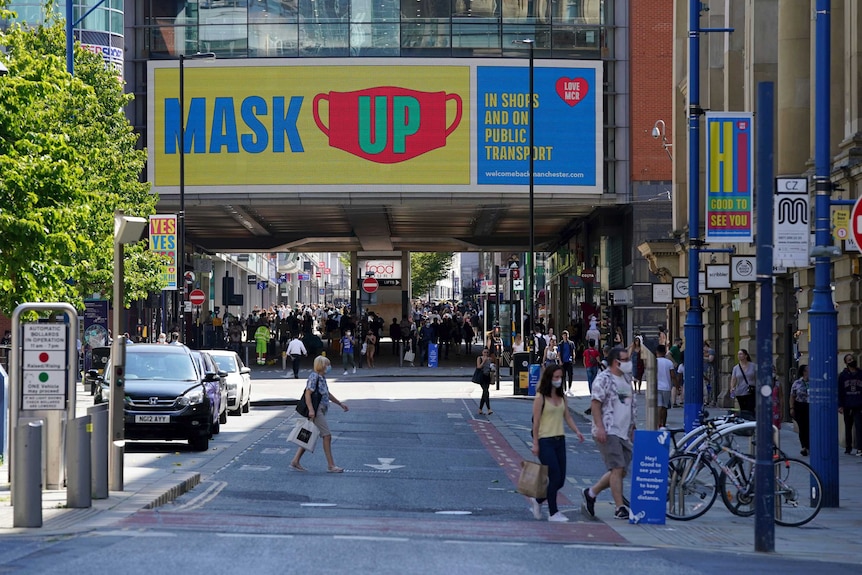 People wearing face masks to try to stop the spread of coronavirus walk backdropped by a "Mask Up" sign in Manchester.