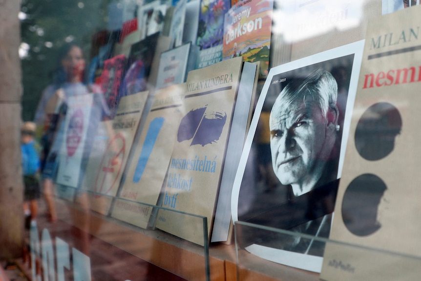 A photo of an older white man is seen alongside books in a shop window. 