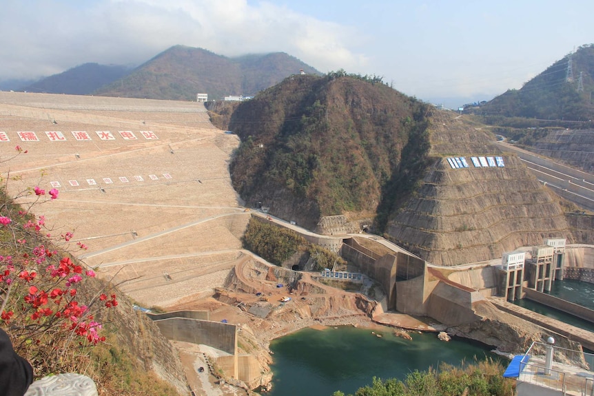 From a high vantage point, you view an incredibly tall dam that is built into the side of a mountain.