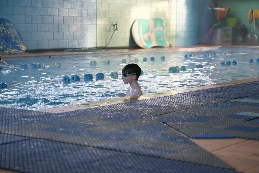 Parker wears goggles in an indoor pool with his head above the water.