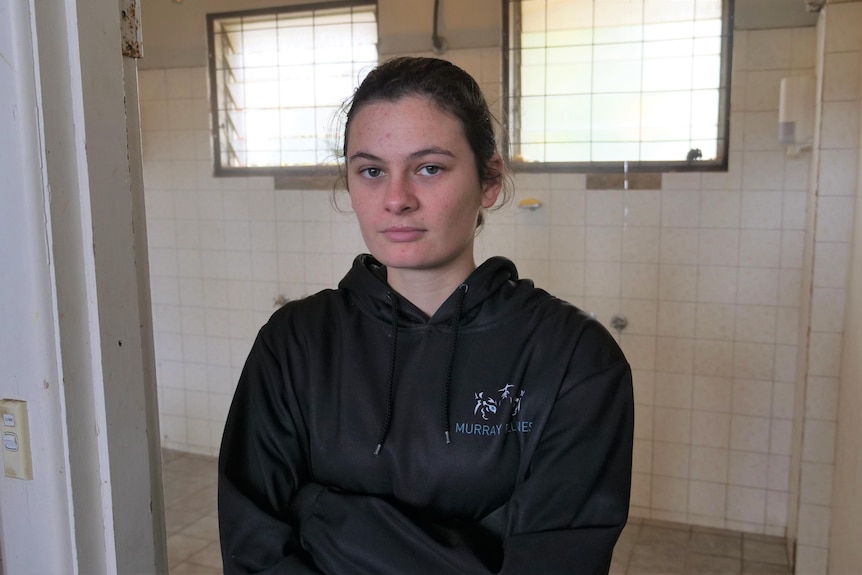 A young woman standing in front of a sports change room shower space