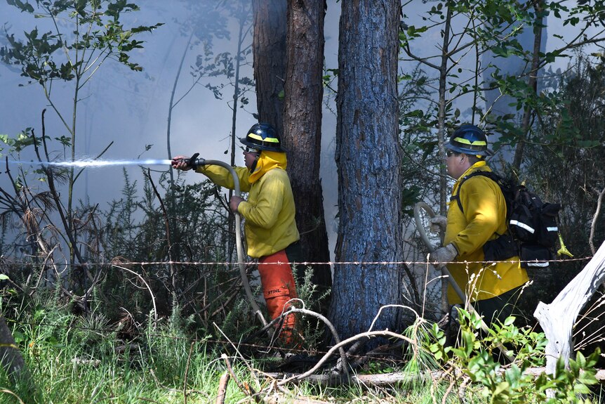 A firefighter holds a hose while another stands behind.