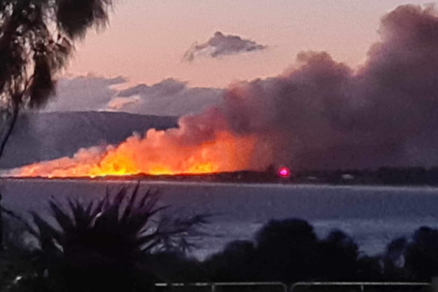 A large bushfire and smoke burns on a beachside spit of land.