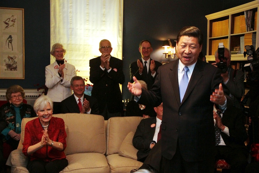 Xi Jinping smiles and gestures in a lounge room as a crowd of older Americans watch and clap