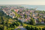 A birds-eye view of a town dotted with houses and a long wall with green fields on one side and the ocean on the other.