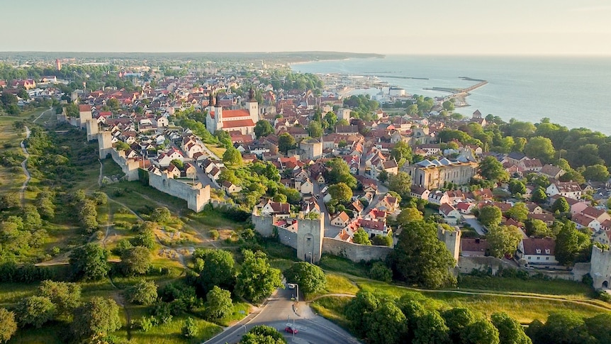 A birds-eye view of a town dotted with houses and a long wall with green fields on one side and the ocean on the other.