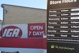 A sign for an IGA shop which says "open 7 days" next to a sign at Woolworths which says the store is closed on Sundays.