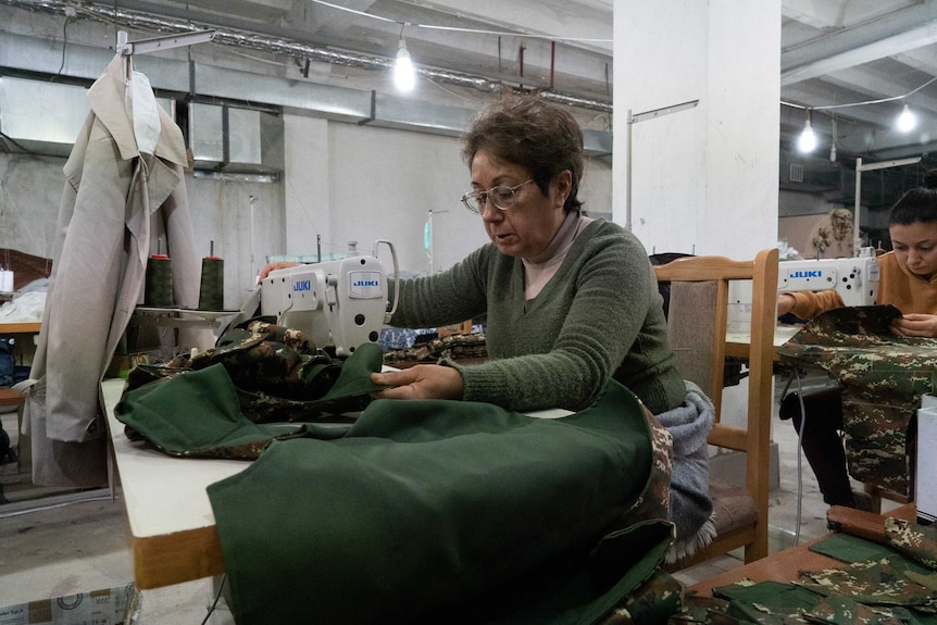 A woman sews green fabric in an industrial room