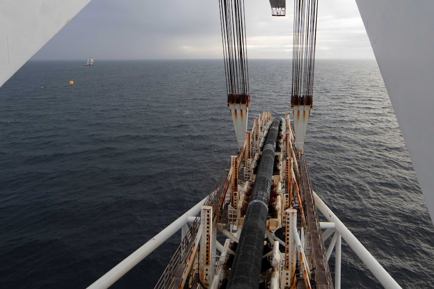 You look down at a black rubber pipe being placed into dark blue sea on an overcast day.