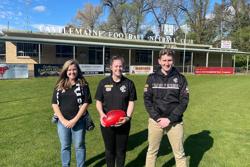 Two women and a man stand in a row in front of the castlemaine football club rooms