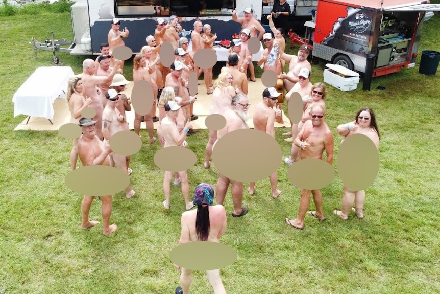 A group of naked festival goers turn and smile for the camera (nudity has been blurred)