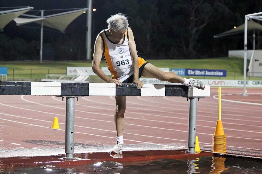 Cecil Walkley on the track climbing over a hurdle.