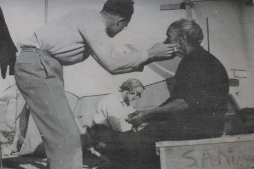 Photo of an old picture of an older aboriginal woman sitting being measured by a white man