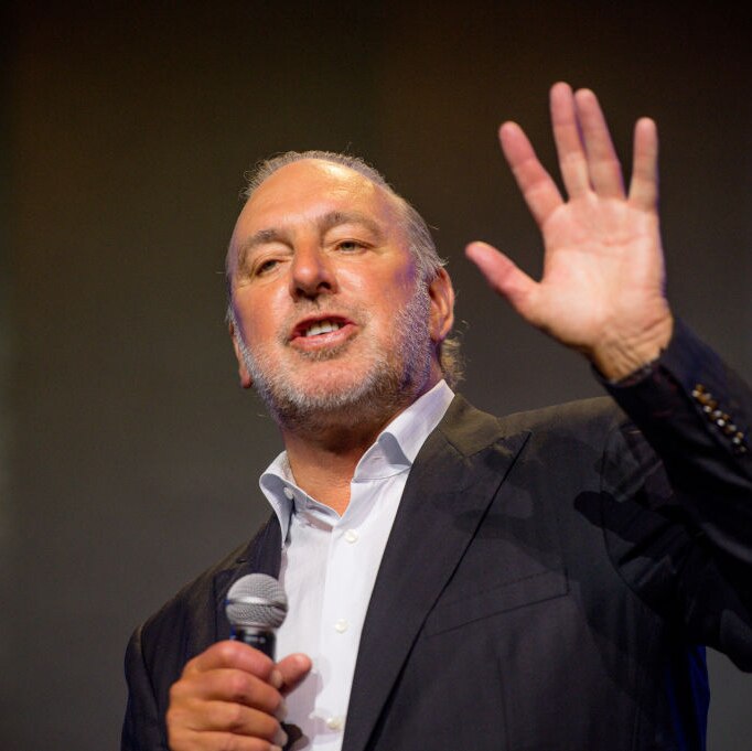 Brian houston wearing suit, preaching with one hand up and another hand holding microphone