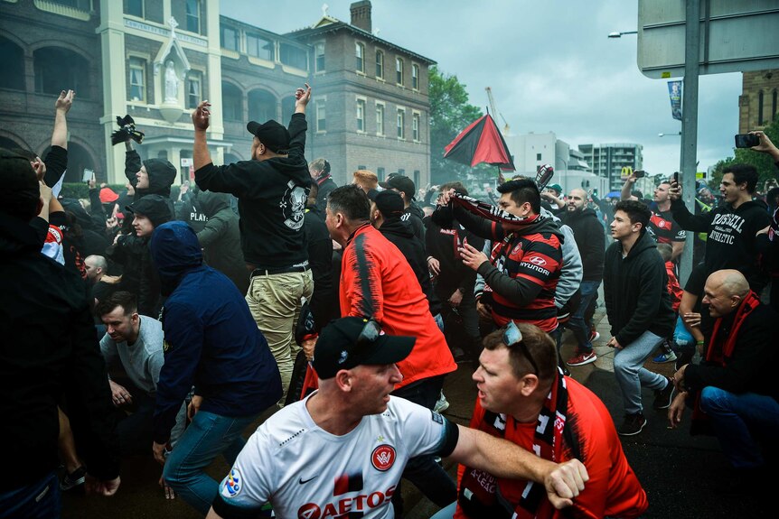 A crowd of men dressed in red and black jump up and down, yelling.