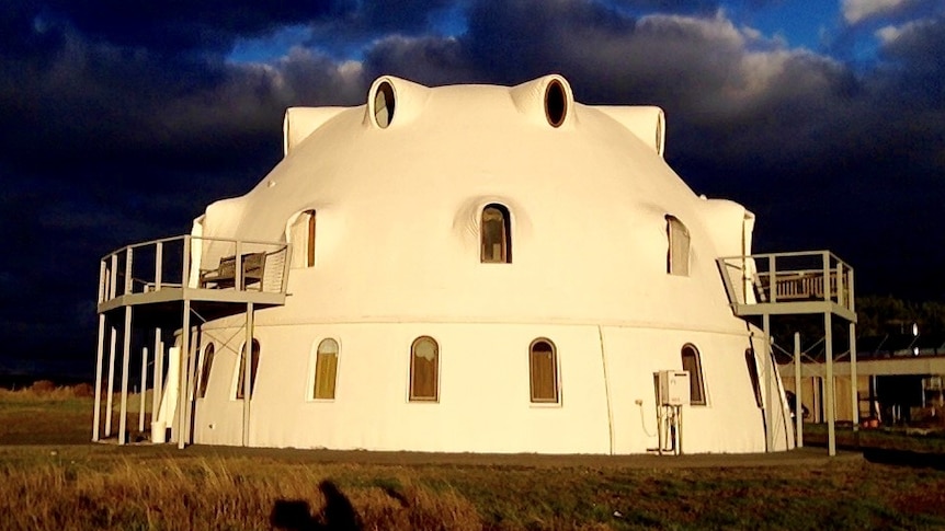 A three story white monolithic dome structure in the sunshine.