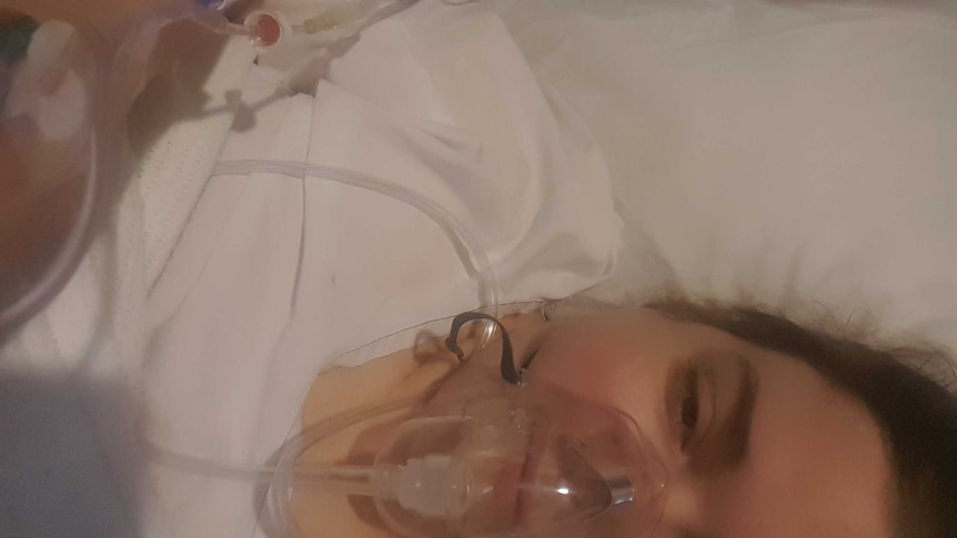 A woman lies in a hospital bed with an oxygen mask