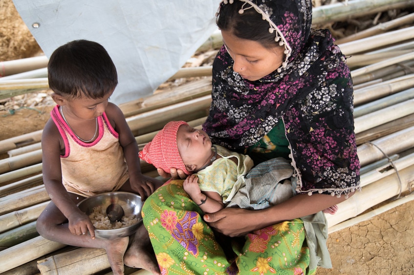 Azida with her young child and four-week-old baby, sitting on the ground.