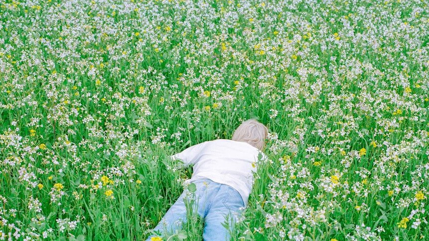 Porter Robinson wearing a white shirt and jeans, laying flat face down in a field of grass and flowers.