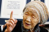 A close up of an elderly woman points upward as she speaks in front of a Guinness World Records certificate.