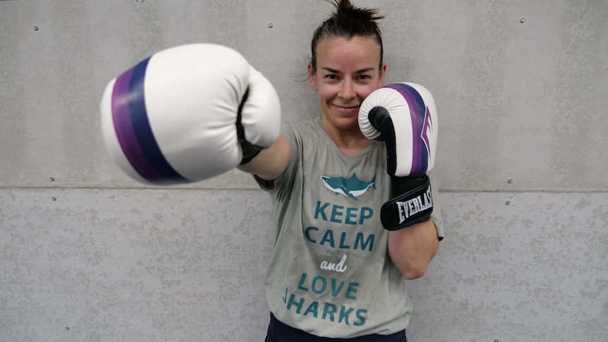 A woman wearing boxing gloves extends one arm towards the camera