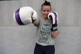 A woman wearing boxing gloves extends one arm towards the camera
