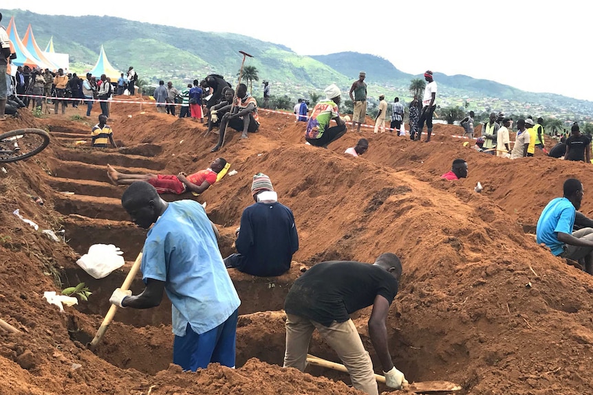 Volunteers are digging a row of graves for victims of the mudslides as locals watch them.