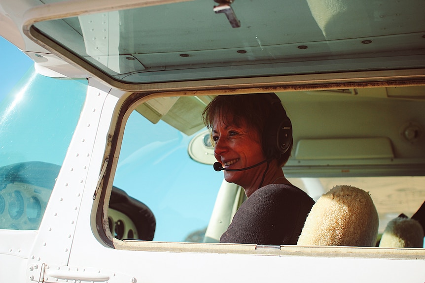 A woman smiles as she sits in a small plane cockpit.