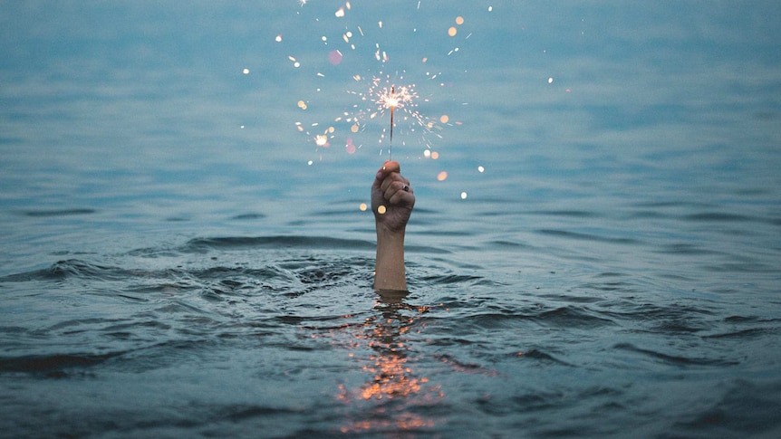 A hand emerging from the sea, holding a lit sparkler