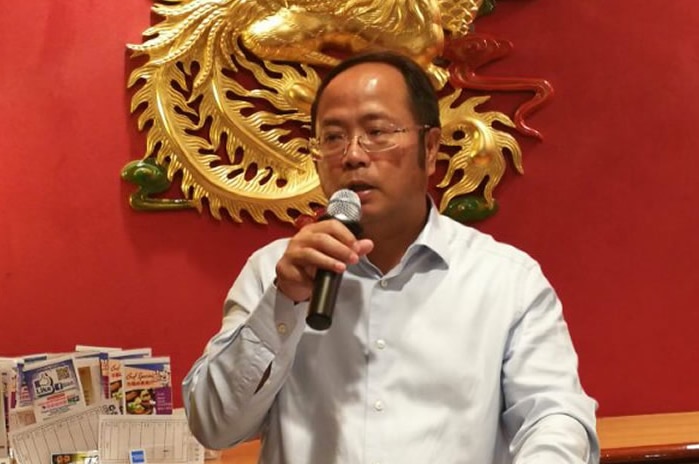 A Chinese man speaks into a microphone at a lectern.