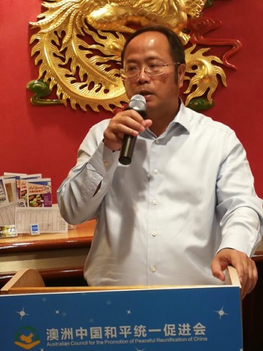 A Chinese man speaks into a microphone at a lectern.