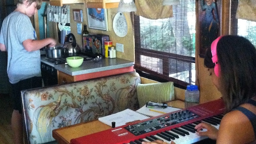 Graciana plays the keyboard a the bus dining table while Banjo prepares food in the adjoining kitchen.