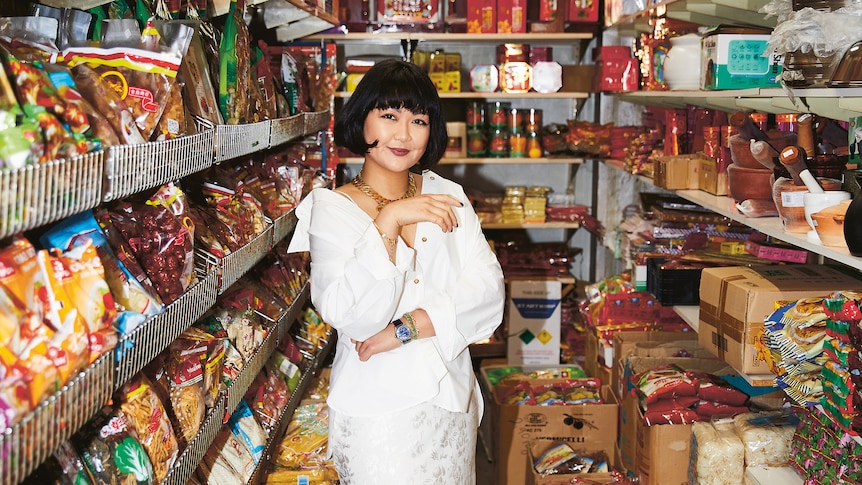 Rosheen Kaul stands smiling in a white dress in the middle of an aisle at a Chinese supermarket.