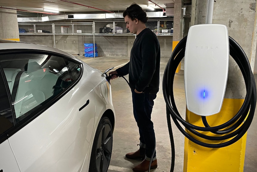 Man standing in a parking lot charging his Tesla. 