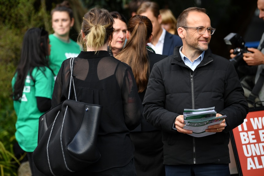 A man holding a stack of papers smiles in a crowd.