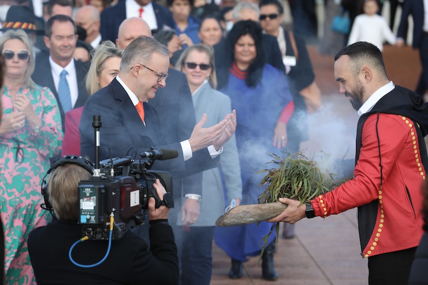 Anthony Albanese holds his arms out in a smoking ceremony outside Parliament House