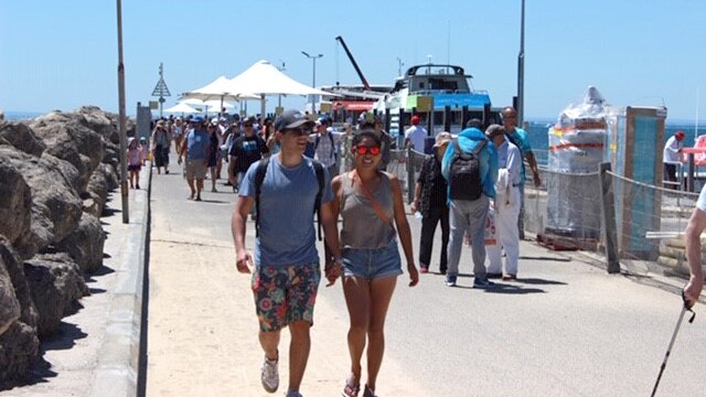 A man and woman hold hands and walk down the Rottnest ferry wharf.