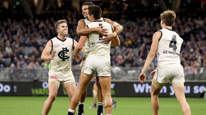 A group of AFL teammates hug and jump around after a goal is scored.
