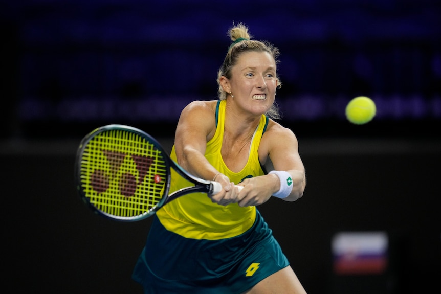 An Australian tennis player grimaces as she stretches to hit a backhand.