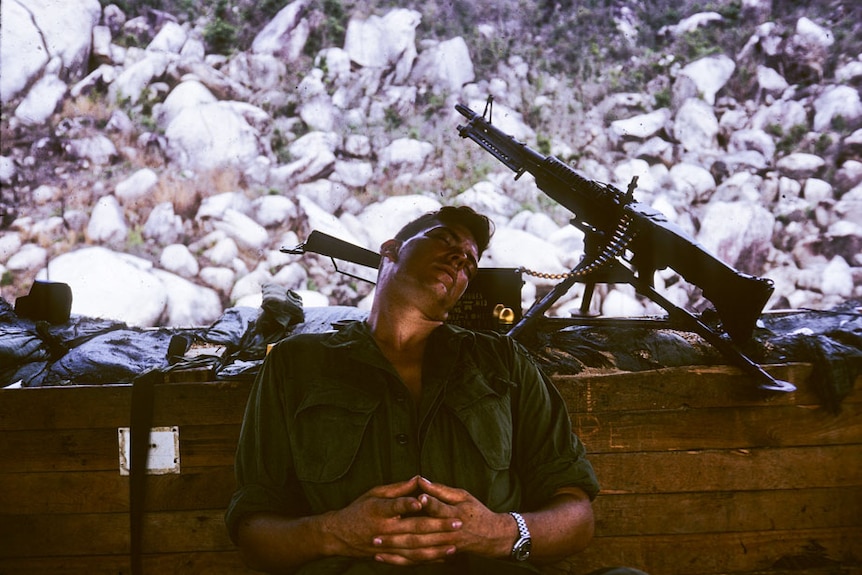 A soldier sleeps next to a machine gun